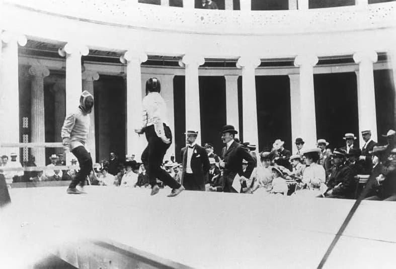 Photograph of a fencing match at the first modern Olympic Games in Athens in 1896, with two fencers on a piste in front of spectators.