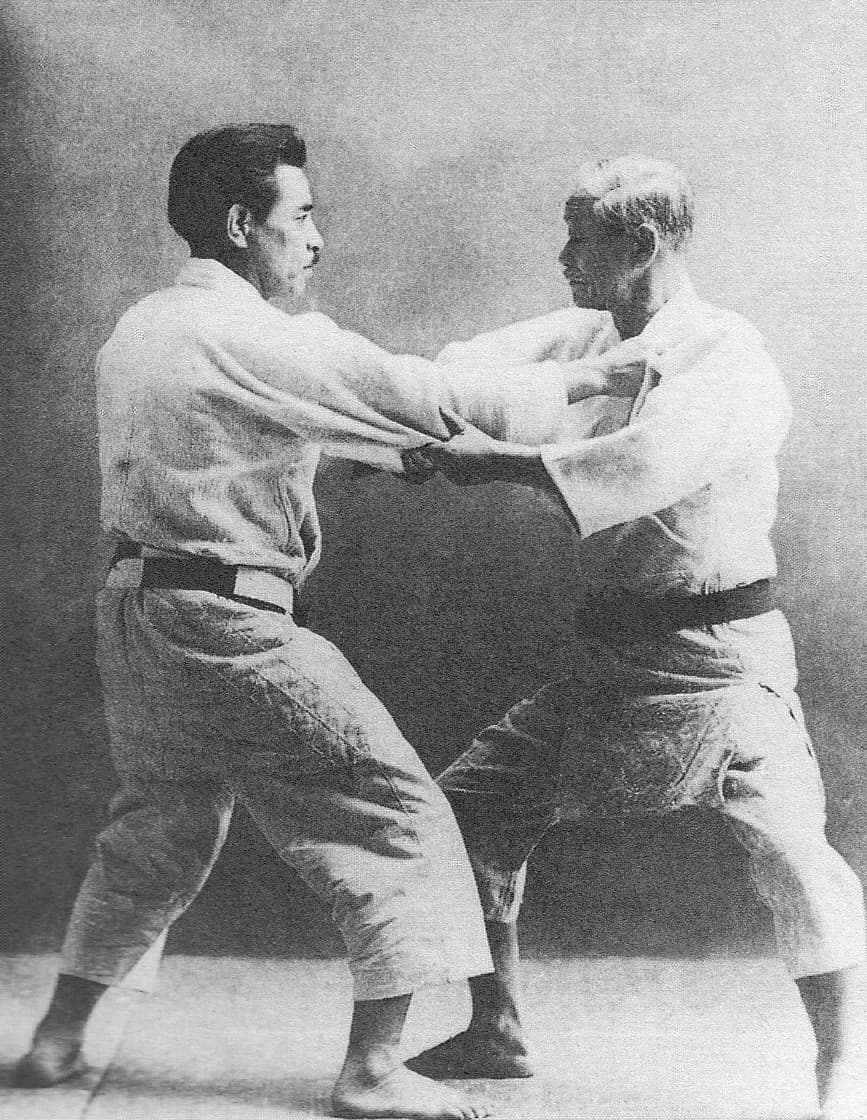 Jigorō Kanō seated in a judogi beside his student Kyūzō Mifune, who stands next to him.