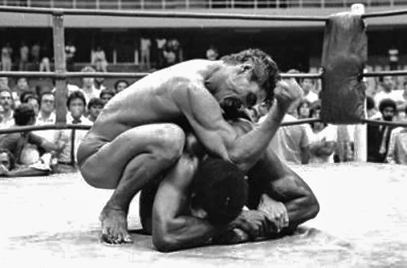 Rickson Gracie in a gi grappling with the much larger Rei Zulu in a ring in Brasília, 1980.