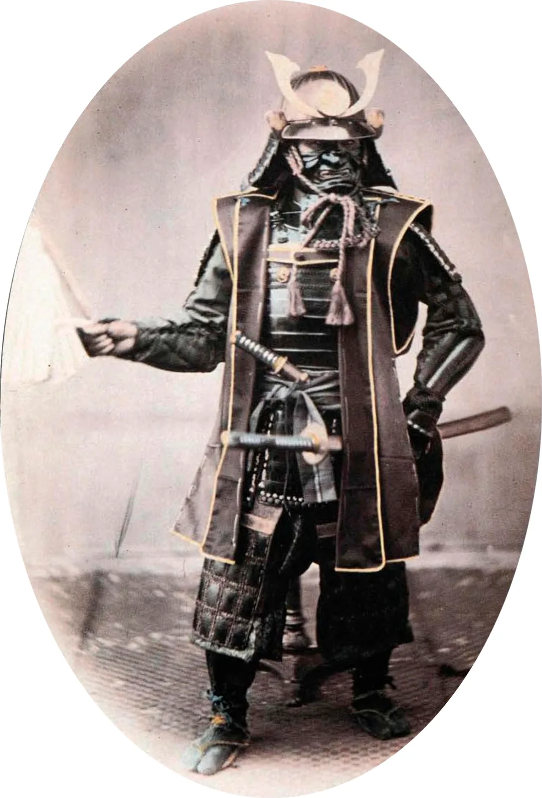 A samurai in full armour with helmet and swords, photographed in a studio in the 1860s.