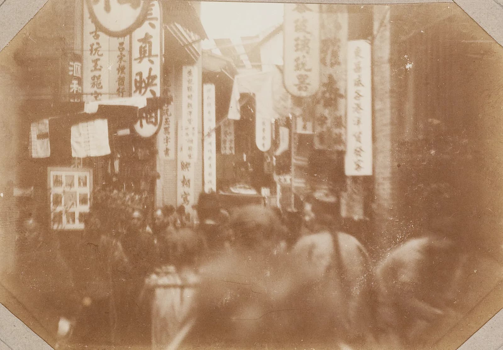 Photograph of a narrow, crowded street in Canton around 1900, lined with shop signs and covered by awnings.