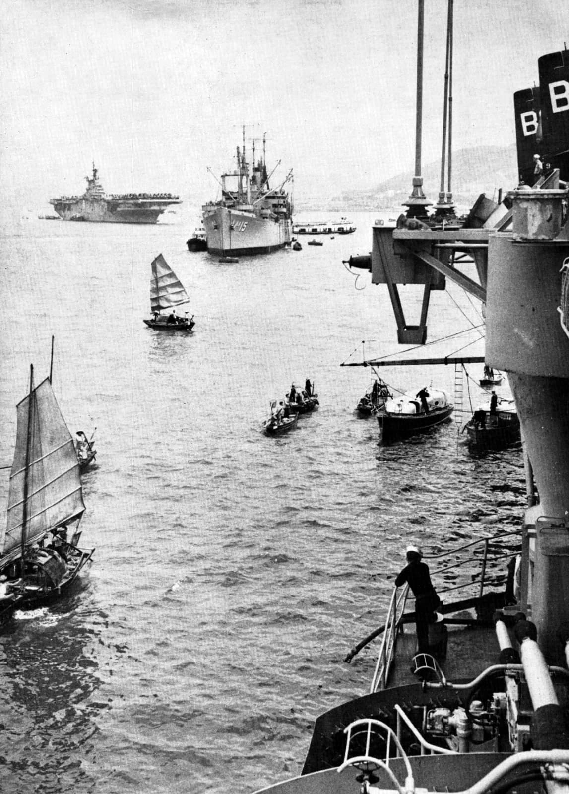 Photograph of Hong Kong harbour around 1954 with a naval ship at anchor and the hills of Kowloon behind.